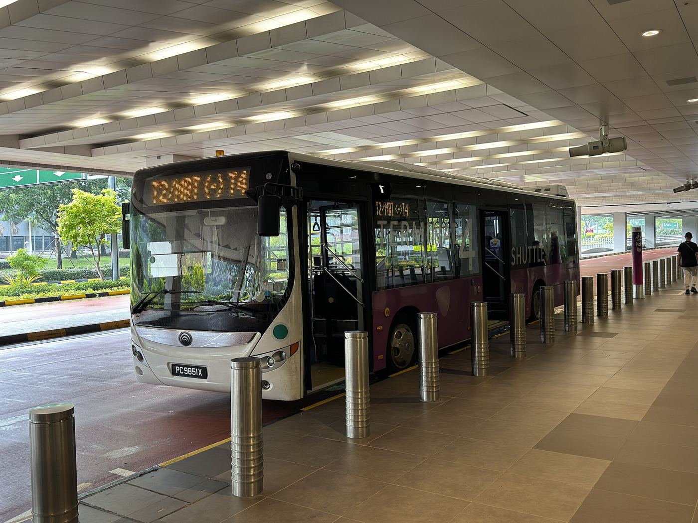 Passengers board an airport shuttle bus outside a busy modern terminal.